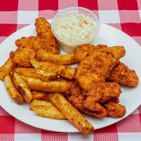 Golden fried chicken tenders with seasoned fries and a side of coleslaw on a white plate over a red and white checkered tablecloth.