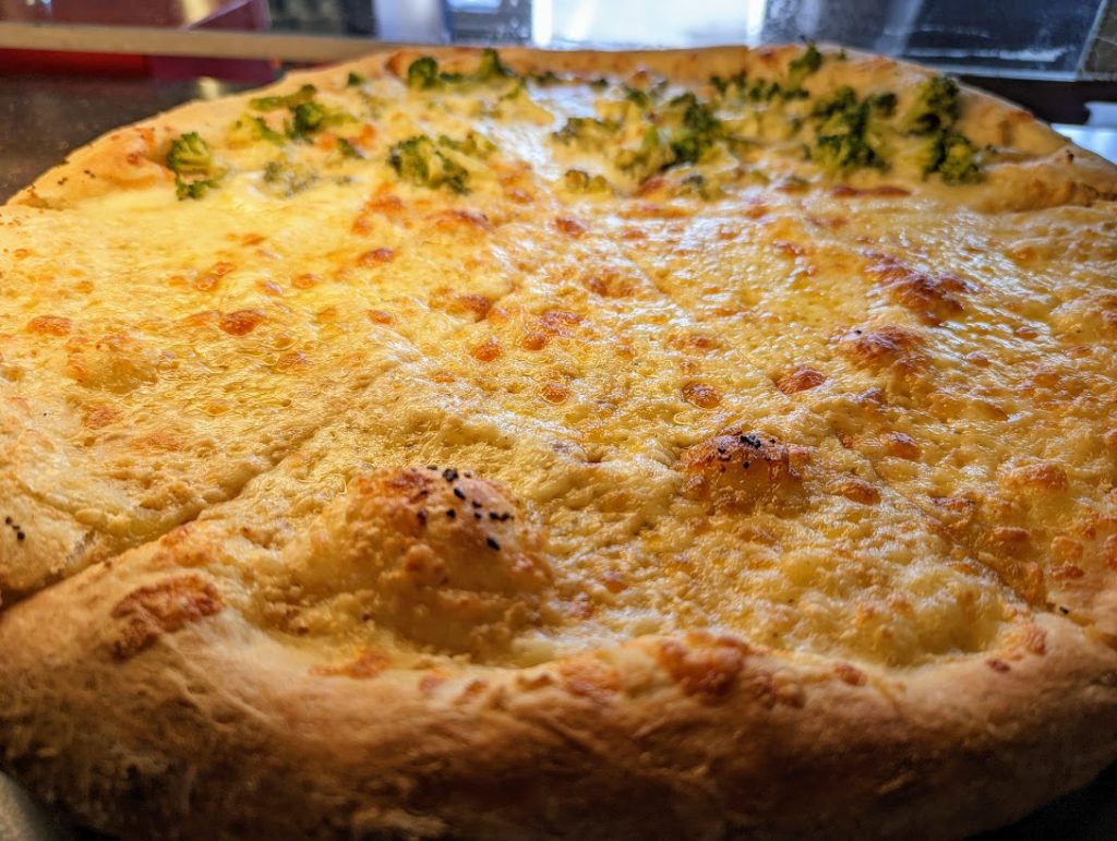A pizza with cheese and broccoli.